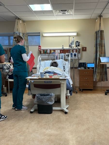 Nursing student performing bedside patient care with SimVS vital signs tablet and simulation manikin