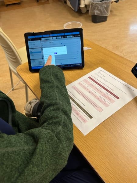 Close-up of SimVS EMR interface on tablet showing patient data and SBAR handoff documentation