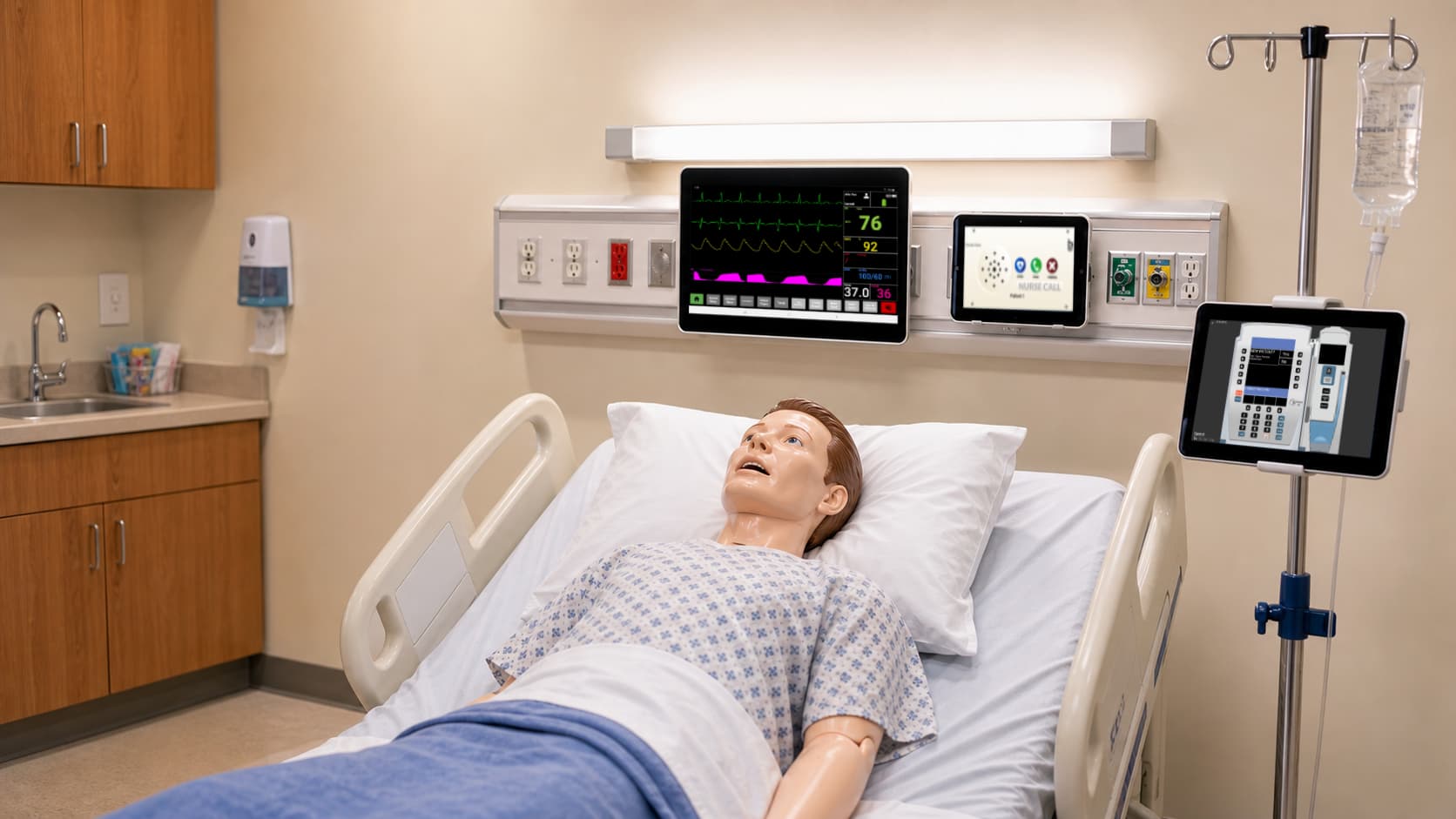 A basic manikin layered with the full SimVS device environment: patient monitor, nurse call, and IV pumps at the bedside.